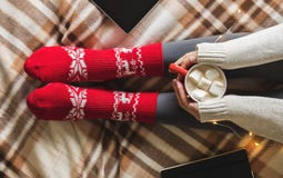 Manos y pies del ` s de las mujeres en el suéter y los calcetines rojos acogedores de lana que sostienen la taza de café caliente foto de archivo libre de regalías Manos y pies del ` s de las mujeres en el suéter y los calcetines rojos acogedores de lana que sostienen la taza de café caliente foto de archivo libre de regalías