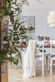 Manta en la silla blanca en la tabla en interior del comedor con las flores y la lámpara de la rota Foto verdadera imagen de archivo libre de regalías Manta en la silla blanca en la tabla en interior del comedor con las flores y la lámpara de la rota Foto verdadera imagen de archivo libre de regalías