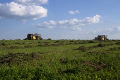 Maquinaria agr?cola, un tractor que recoge la hierba en un campo contra un cielo azul Haga heno la cosecha, cosecha de la hierba foto de archivo libre de regalías Maquinaria agr?cola, un tractor que recoge la hierba en un campo contra un cielo azul Haga heno la cosecha, cosecha de la hierba foto de archivo libre de regalías