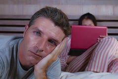 Mari fâché et frustrant déprimé dans le lit ignoré par son amie sociale d'épouse de bourreau de travail ou d'intoxiqué de médias photographie stock Mari fâché et frustrant déprimé dans le lit ignoré par son amie sociale d'épouse de bourreau de travail ou d'intoxiqué de médias photographie stock