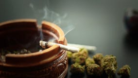 Marijuana Joint Burning 2. A marijuana filled joint burning on the edge of a wooden ashtray. More marijuana to the side Marijuana Joint Burning 2. A marijuana filled joint burning on the edge of a wooden ashtray. More marijuana to the side
