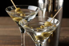 Martini i en exponeringsglasvinglas med gröna oliv på en steknål på en brun trätabell coctailar stång arkivbilder Martini i en exponeringsglasvinglas med gröna oliv på en steknål på en brun trätabell coctailar stång arkivbilder
