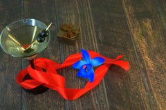 Martini γυαλί με τις ελιές με την ερυθρά κορδέλλα, το κιβώτιο δώρων και την μπλε ορχιδέα σε έναν ξύλινο πίνακα στοκ εικόνα Martini γυαλί με τις ελιές με την ερυθρά κορδέλλα, το κιβώτιο δώρων και την μπλε ορχιδέα σε έναν ξύλινο πίνακα στοκ εικόνα