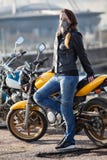 Mascarilla del cuello del motorista de la mujer que lleva joven que presenta detrás de su bici de la calle al aire libre Fotos de archivo libres de regalías Mascarilla del cuello del motorista de la mujer que lleva joven que presenta detrás de su bici de la calle al aire libre Fotos de archivo libres de regalías