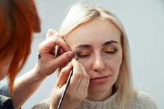 Maskenbildner mit einer Bürste in den Händen mit einem flachen Rand malt den Pfeil auf dem Augenlid des Modells, anwendet Make-up stockbilder Maskenbildner mit einer Bürste in den Händen mit einem flachen Rand malt den Pfeil auf dem Augenlid des Modells, anwendet Make-up stockbilder