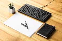 Materiale dell'ufficio con un taccuino, un foglio di carta, penna, tastiera su una tavola di legno immagini stock Materiale dell'ufficio con un taccuino, un foglio di carta, penna, tastiera su una tavola di legno immagini stock