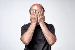 Mature caucasian man in black t-shirt covering his face with hands over gray background. Royalty Free Stock Photography Mature caucasian man in black t-shirt covering his face with hands over gray background. Royalty Free Stock Photography