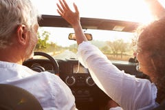 Mature Couple Driving Along Country Road In Open Top Car