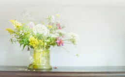 Mazzo dei fiori selvaggi in vaso di vetro sullo scaffale di legno a fondo leggero Decorazione domestica floreale fotografia stock Mazzo dei fiori selvaggi in vaso di vetro sullo scaffale di legno a fondo leggero Decorazione domestica floreale fotografia stock