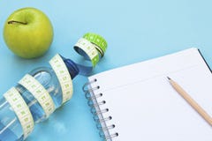 Maçã fresca, fita de medição, garrafa de água e caderno no fundo azul imagens de stock Maçã fresca, fita de medição, garrafa de água e caderno no fundo azul imagens de stock