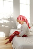 Mały blondynki dziecko w Bożenarodzeniowym kapeluszu siedzi na łóżku z białymi bedclothes, sztuki z magiczną różdżką, poważny sko fotografia royalty free Mały blondynki dziecko w Bożenarodzeniowym kapeluszu siedzi na łóżku z białymi bedclothes, sztuki z magiczną różdżką, poważny sko fotografia royalty free