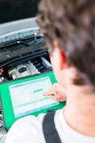 Meccanico con lo strumento diagnostico nell'officina dell'automobile immagine stock libera da diritti Meccanico con lo strumento diagnostico nell'officina dell'automobile immagine stock libera da diritti