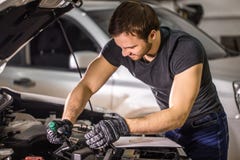 Mechanik pracuje pod samochodowym kapiszonem w remontowym garażu zdjęcie stock Mechanik pracuje pod samochodowym kapiszonem w remontowym garażu zdjęcie stock
