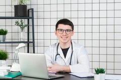 Medicina, profissão, tecnologia e conceito dos povos - doutor masculino de sorriso com o portátil no escritório médico imagens de stock royalty free Medicina, profissão, tecnologia e conceito dos povos - doutor masculino de sorriso com o portátil no escritório médico imagens de stock royalty free