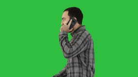 Cool young man with beard walking and talking with mobile phone on a Green Screen, Chroma Key.