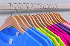 Mehrfarbige Frauen ` s T-Shirts hängen an den hölzernen Aufhängern lizenzfreie stockfotos Mehrfarbige Frauen ` s T-Shirts hängen an den hölzernen Aufhängern lizenzfreie stockfotos