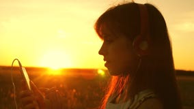 Meisjesreiziger die aan muziek op smartphone in stralen van een mooie de lentezonsondergang luisteren jong meisje met hoofdtelefo stock footage Meisjesreiziger die aan muziek op smartphone in stralen van een mooie de lentezonsondergang luisteren jong meisje met hoofdtelefo stock footage
