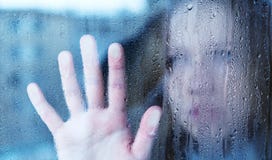 Melancholische und traurige junge Frau am Fenster im Regen stockbild Melancholische und traurige junge Frau am Fenster im Regen stockbild