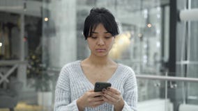 Mellersta skott av den asiatiska kvinnlign som går med en telefon på fönsterbakgrund Mellersta skott av den asiatiska kvinnlign som går med en telefon på fönsterbakgrund