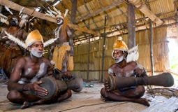 Men Asmat tribe are sitting at home and play on the drum.