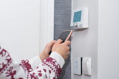 A menina ajusta e regula a temperatura ambiente com o telefone esperto na parede do interruptor foto de stock A menina ajusta e regula a temperatura ambiente com o telefone esperto na parede do interruptor foto de stock