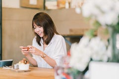 Menina asiática bonita que toma a foto de sobremesas doces na cafetaria, usando a câmera do smartphone, afixando em meios sociais imagem de stock Menina asiática bonita que toma a foto de sobremesas doces na cafetaria, usando a câmera do smartphone, afixando em meios sociais imagem de stock