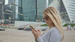 Menina bonita do louro no uso dos óculos de sol do telefone celular na perspectiva do centro da cidade filme Menina bonita do louro no uso dos óculos de sol do telefone celular na perspectiva do centro da cidade filme