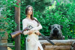 Menina bonita no vestido branco que levanta com um rifle de caça e um varrão enchido no fundo imagens de stock Menina bonita no vestido branco que levanta com um rifle de caça e um varrão enchido no fundo imagens de stock