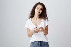 A menina bonita recebe o cumprimento ao estar na fila que consulta no smartphone Mulher encaracolado-de cabelo à moda atrativa fotografia de stock royalty free A menina bonita recebe o cumprimento ao estar na fila que consulta no smartphone Mulher encaracolado-de cabelo à moda atrativa fotografia de stock royalty free
