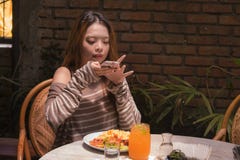 Menina coreana asiática bonita e feliz nova do estudante que senta-se na cafetaria doce que toma a foto de sua refeição com câmer imagem de stock royalty free Menina coreana asiática bonita e feliz nova do estudante que senta-se na cafetaria doce que toma a foto de sua refeição com câmer imagem de stock royalty free
