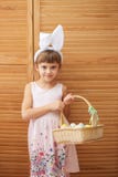 A menina de encantamento no vestido com as orelhas de coelho brancas em sua cabeça guarda uma cesta com os ovos tingidos no imagens de stock A menina de encantamento no vestido com as orelhas de coelho brancas em sua cabeça guarda uma cesta com os ovos tingidos no imagens de stock