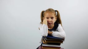 A menina de primeiro grau da escola senta a inclinação em livros com um olhar cansado Um estudante cansado com livros olha a câme video estoque A menina de primeiro grau da escola senta a inclinação em livros com um olhar cansado Um estudante cansado com livros olha a câme video estoque