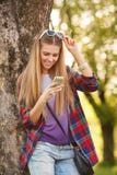 Menina de sorriso atrativa que texting no telefone celular, exterior Mulher feliz moderna com um smartphone Imagens de Stock Royalty Free Menina de sorriso atrativa que texting no telefone celular, exterior Mulher feliz moderna com um smartphone Imagens de Stock Royalty Free