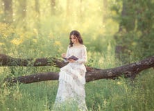 A menina doce de encantamento com cabelo escuro e os ombros desencapados em um vestido branco do vintage lindo senta-se em uma ár fotografia de stock A menina doce de encantamento com cabelo escuro e os ombros desencapados em um vestido branco do vintage lindo senta-se em uma ár fotografia de stock