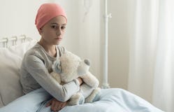 Menina doente triste com o lenço cor-de-rosa que abraça o brinquedo do luxuoso no hospital imagens de stock Menina doente triste com o lenço cor-de-rosa que abraça o brinquedo do luxuoso no hospital imagens de stock
