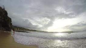 A menina em um roupa de banho corre ao longo da praia no por do sol no movimento lento, Bali vídeos de arquivo A menina em um roupa de banho corre ao longo da praia no por do sol no movimento lento, Bali vídeos de arquivo