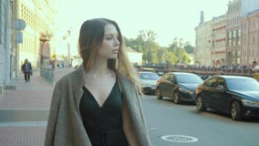 A menina encantador em um fato-macaco elegante do cocktail vai ao longo de uma rua da cidade no slo-mo filme A menina encantador em um fato-macaco elegante do cocktail vai ao longo de uma rua da cidade no slo-mo filme