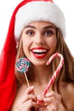 A menina feliz com bordos vermelhos e no chapéu do Natal está guardando o pirulito e o sorriso do Natal dois Isolado Fotos de Stock A menina feliz com bordos vermelhos e no chapéu do Natal está guardando o pirulito e o sorriso do Natal dois Isolado Fotos de Stock