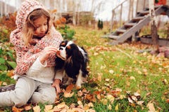 Menina feliz da criança que joga com seu cão descuidado do spaniel de rei Charles no outono imagens de stock Menina feliz da criança que joga com seu cão descuidado do spaniel de rei Charles no outono imagens de stock