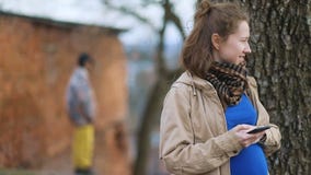 Menina grávida dos jovens no revestimento retro do vintage bege usando seu smartphone, homem misterioso na calças amarela que est video estoque Menina grávida dos jovens no revestimento retro do vintage bege usando seu smartphone, homem misterioso na calças amarela que est video estoque