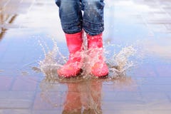 A menina nas botas cor-de-rosa que saltam nas poças fotografia de stock A menina nas botas cor-de-rosa que saltam nas poças fotografia de stock