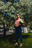 Menina nos óculos de sol e em vidros cor-de-rosa da camiseta com entre as árvores de florescência fotos de stock Menina nos óculos de sol e em vidros cor-de-rosa da camiseta com entre as árvores de florescência fotos de stock