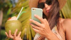 Menina nova do moderno da raça misturada que Texting no telefone celular e no cocktail bebendo do coco na praia tropical 4K, Slow vídeos de arquivo Menina nova do moderno da raça misturada que Texting no telefone celular e no cocktail bebendo do coco na praia tropical 4K, Slow vídeos de arquivo