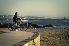A menina nova e bonita está montando uma bicicleta pelo cais ao lado do Oceano Atlântico imagem de stock A menina nova e bonita está montando uma bicicleta pelo cais ao lado do Oceano Atlântico imagem de stock