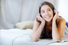 Menina que escuta os fones de ouvido colocados na cama imagem de stock royalty free Menina que escuta os fones de ouvido colocados na cama imagem de stock royalty free