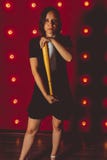 Menina que levanta em um fundo vermelho com um bastão de beisebol em suas mãos, no conceito de uma intimidação ou em atletas imagem de stock Menina que levanta em um fundo vermelho com um bastão de beisebol em suas mãos, no conceito de uma intimidação ou em atletas imagem de stock