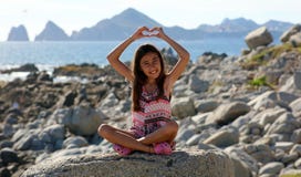 Menina que senta-se em rochas na parte dianteira de oceano no mar do penhasco do recurso de Los Cabos México imagens de stock Menina que senta-se em rochas na parte dianteira de oceano no mar do penhasco do recurso de Los Cabos México imagens de stock