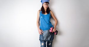 A menina que 'sexy' o jaque de todos os comércios está contra a parede branca e realiza em suas mãos uma chave de fenda amarela foto de stock royalty free A menina que 'sexy' o jaque de todos os comércios está contra a parede branca e realiza em suas mãos uma chave de fenda amarela foto de stock royalty free