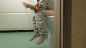 A menina senta-se no toalete e usa-se o telefone video estoque A menina senta-se no toalete e usa-se o telefone video estoque