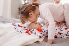 A menina vestida no pijama beija seu irmão minúsculo que encontra-se na cama fotografia de stock A menina vestida no pijama beija seu irmão minúsculo que encontra-se na cama fotografia de stock